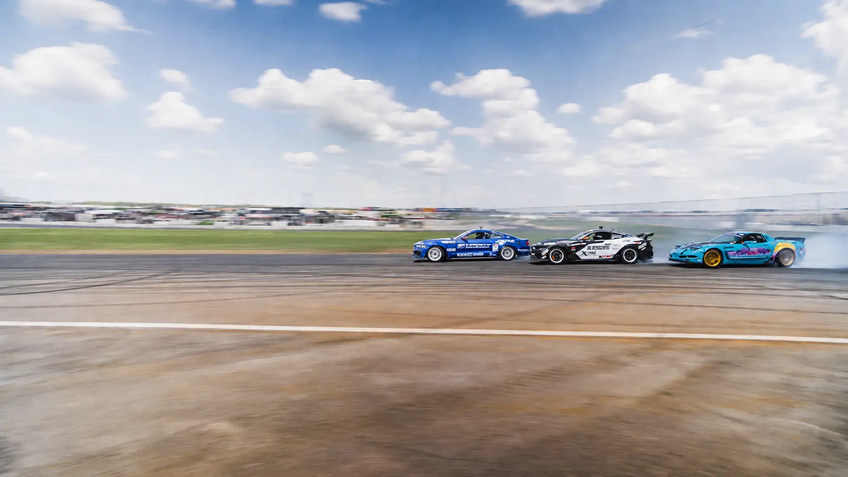 Three drift cars running a close tandem chase through tire smoke