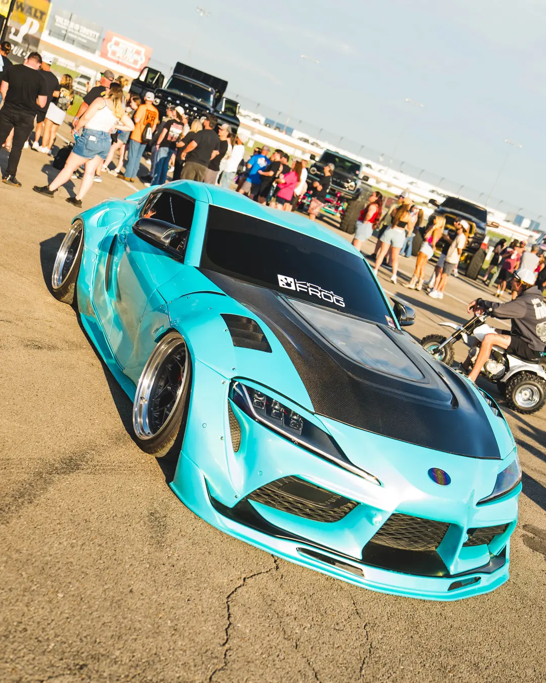 Turquoise widebody show car surrounded by automotive fans